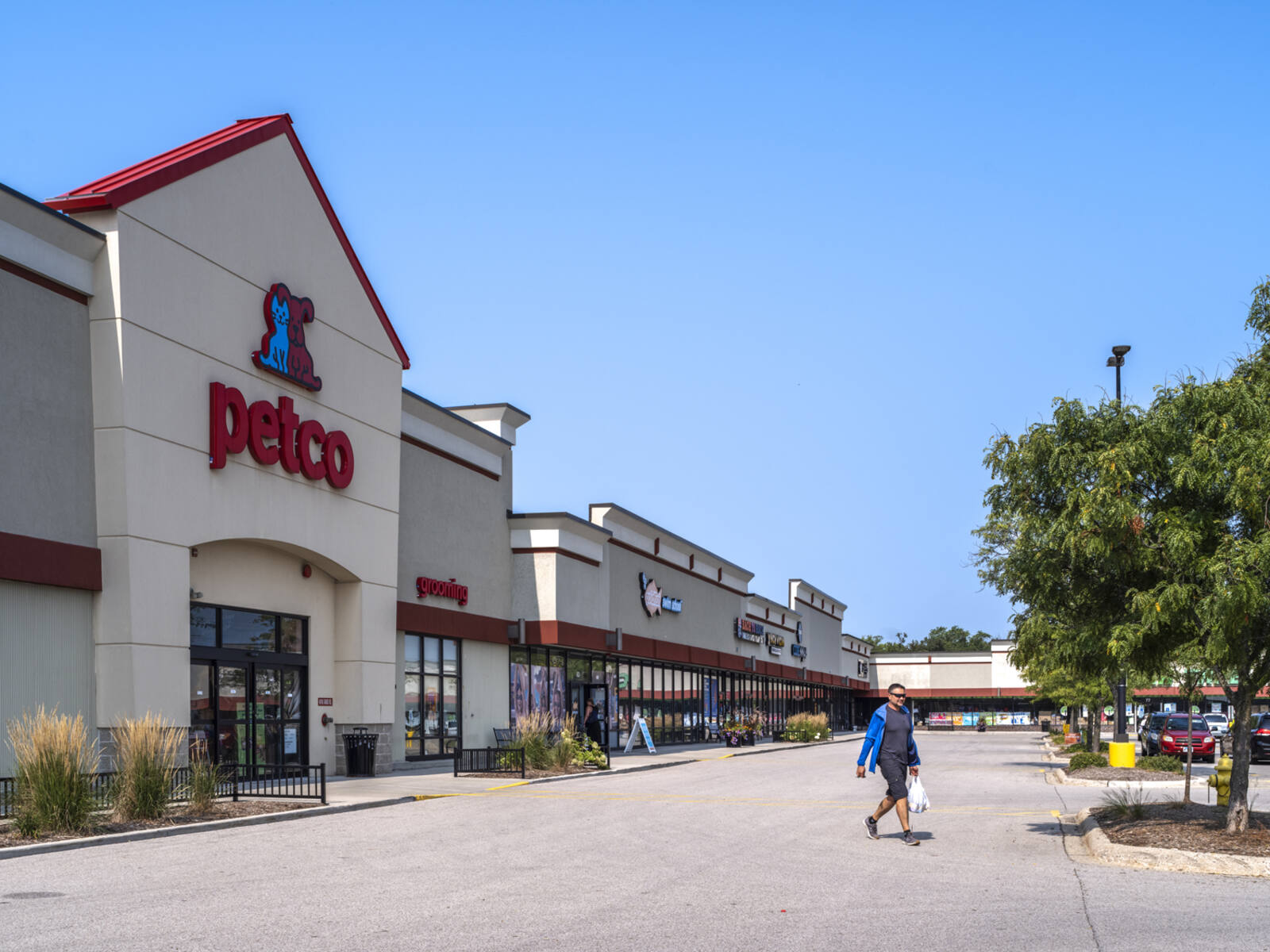 Customer exiting Petco into tree-lined parking lot.