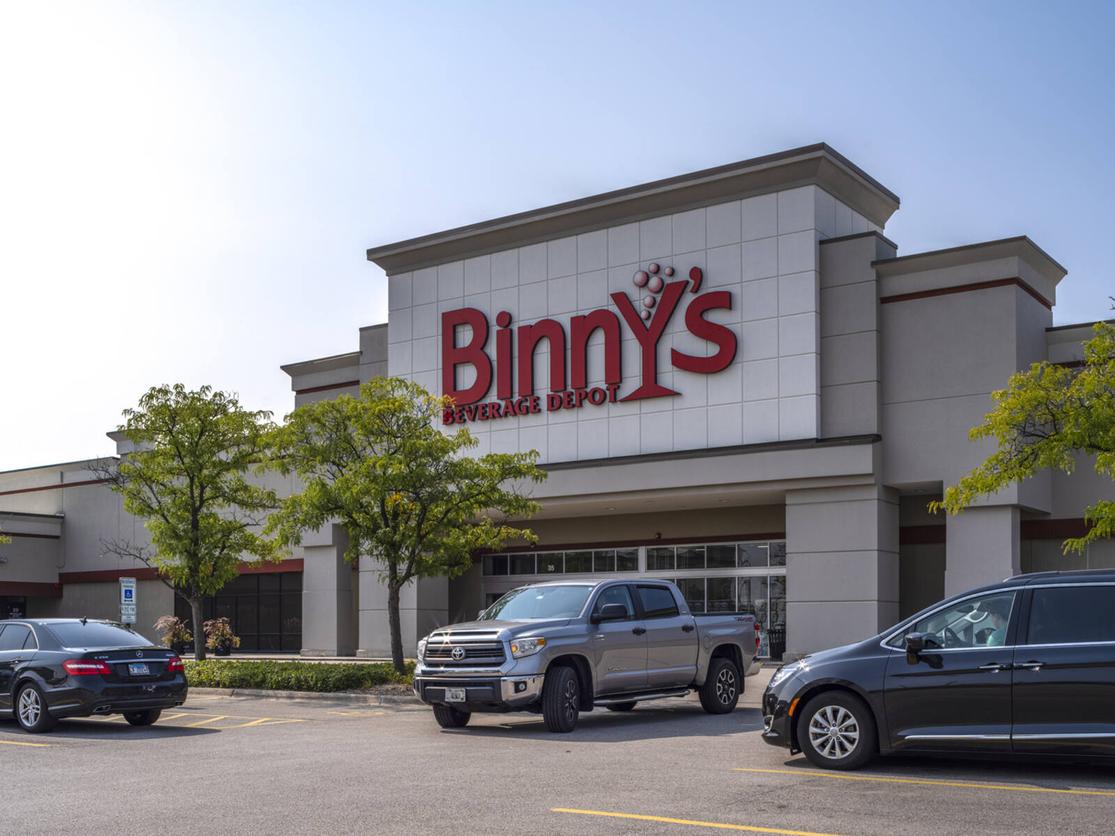 Jeep turns in front of Binny's beverage center lined with small trees.