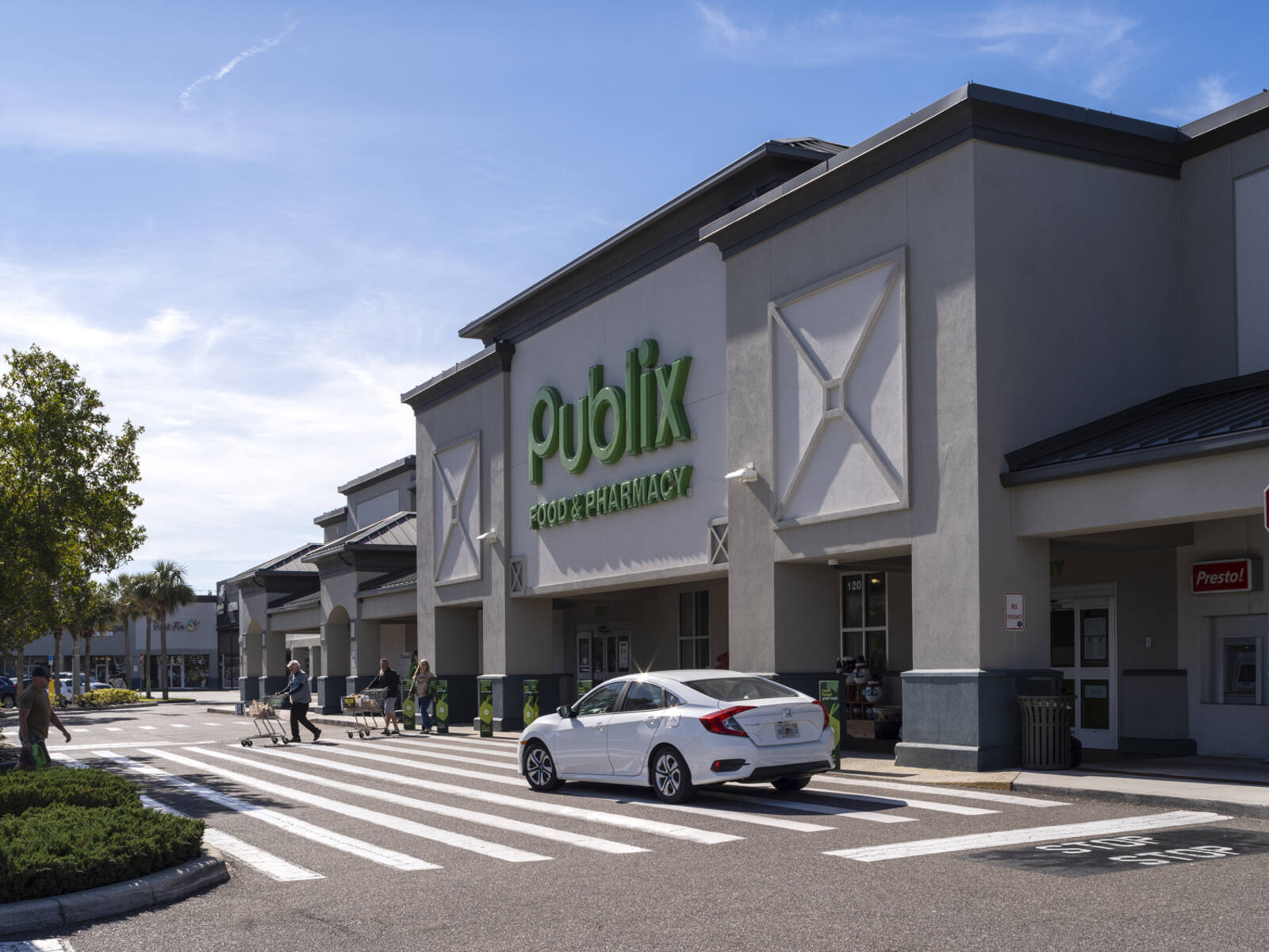 White car and patrons in crosswalk of Publix grocer.