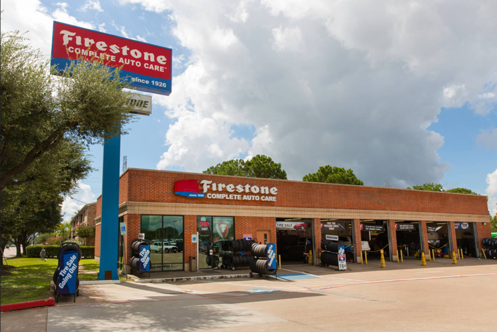 Firestone auto shop with large tree in front and grey clouds behind.