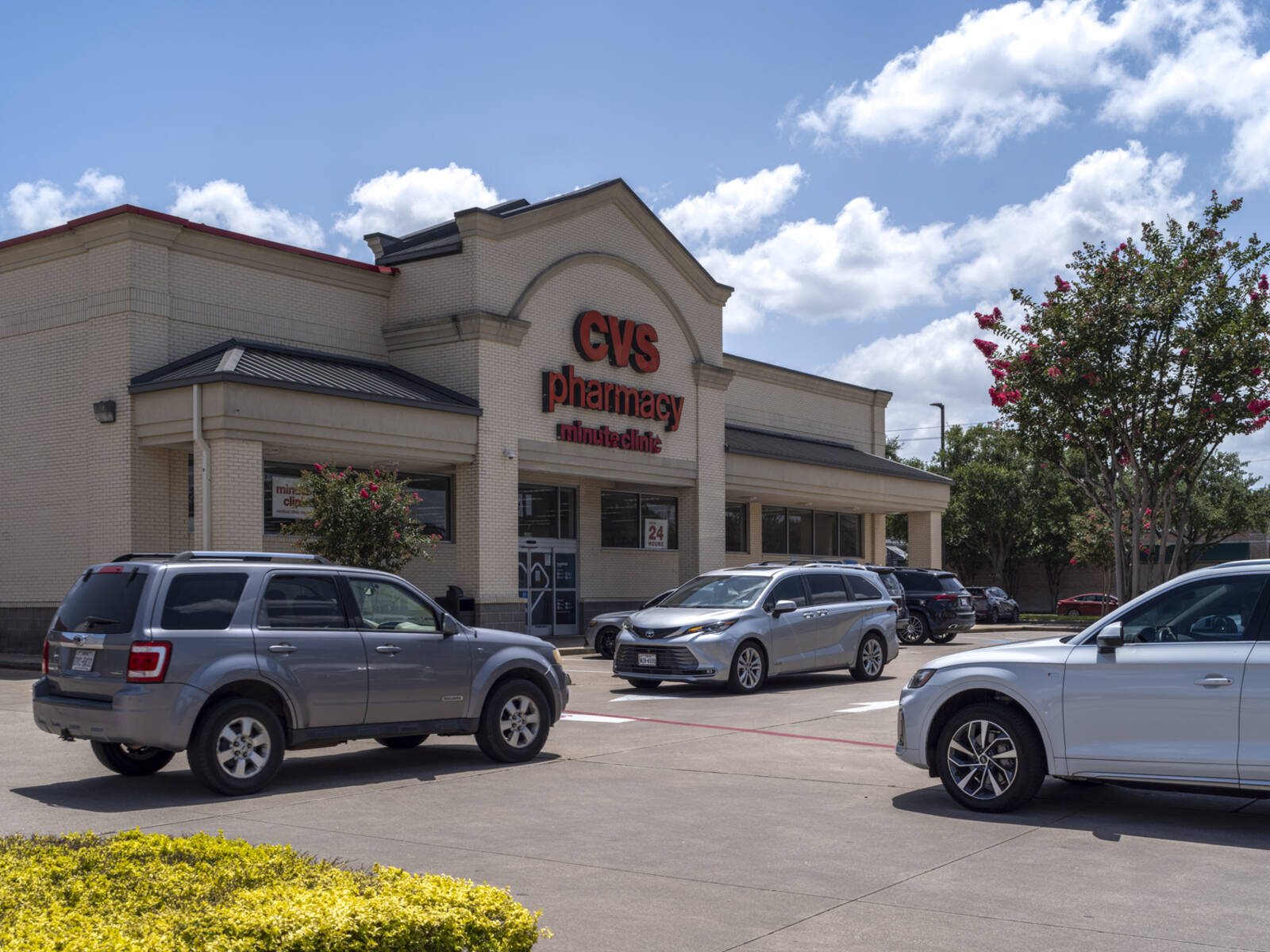 CVS Pharmacy with 3 grey SUVS at an intersection in front.