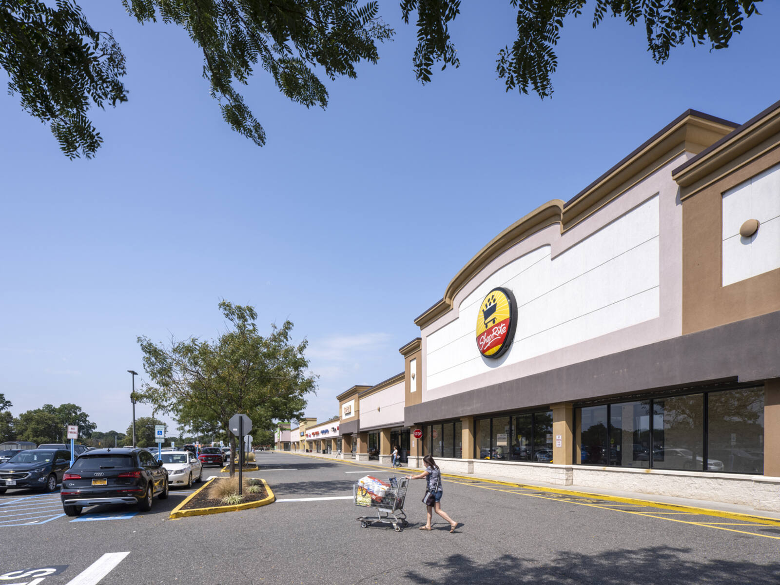Woman pushing cart filled with groceries exits ShopRite to the parking lot.