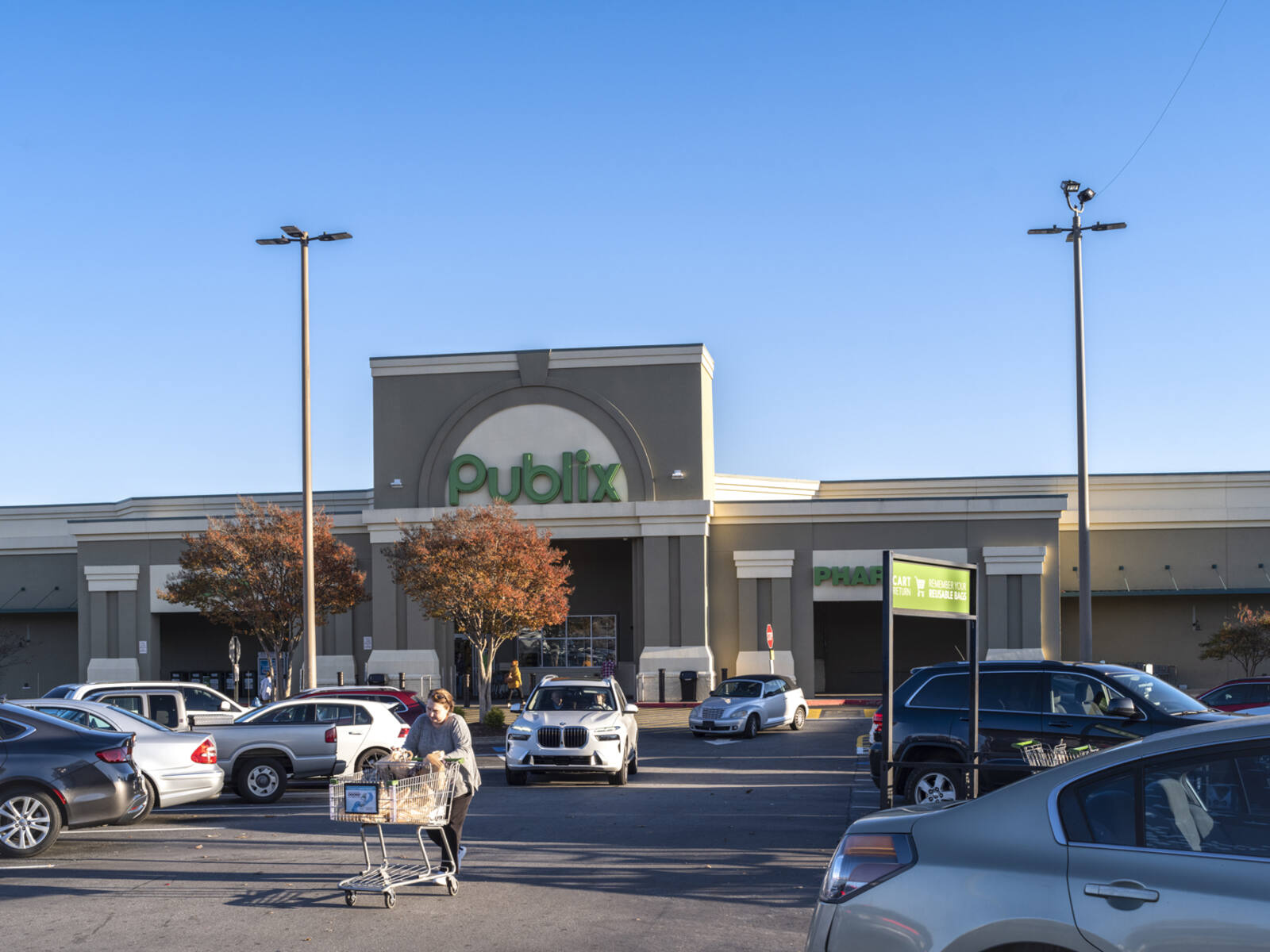 Woman with carriage walking up busy parking lot in front of Publix grocery store.