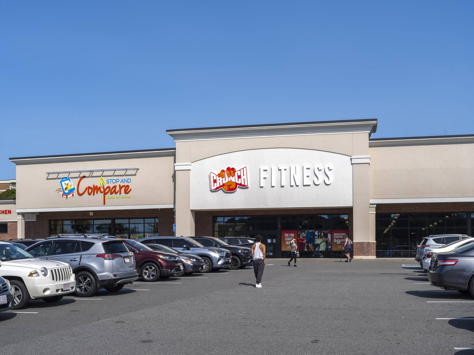 Patrons walking up parking lot aisle in front of Crunch Fitness.