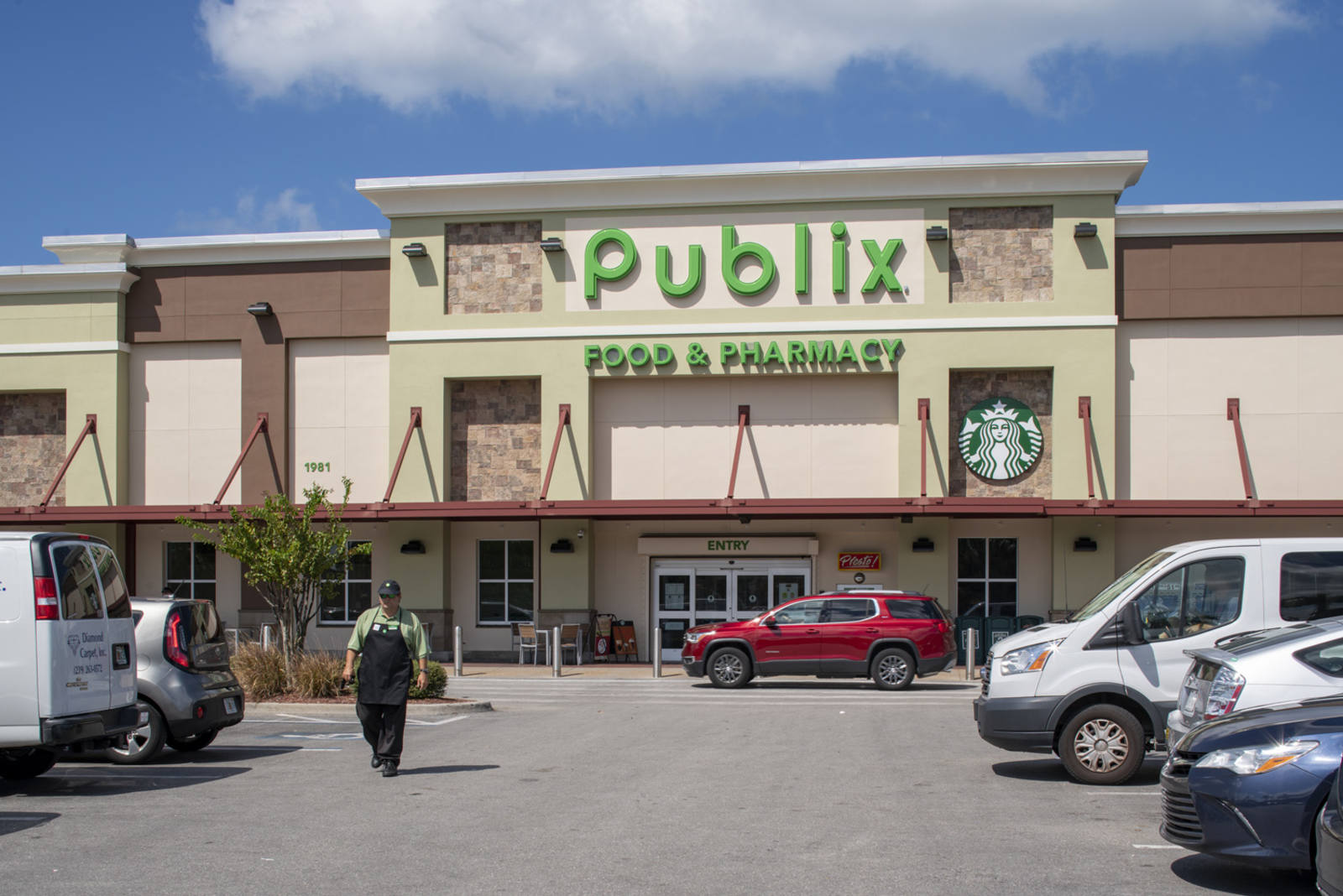 Employee in apron exiting Publix supermarket into the parking lot at Naples Plaza.