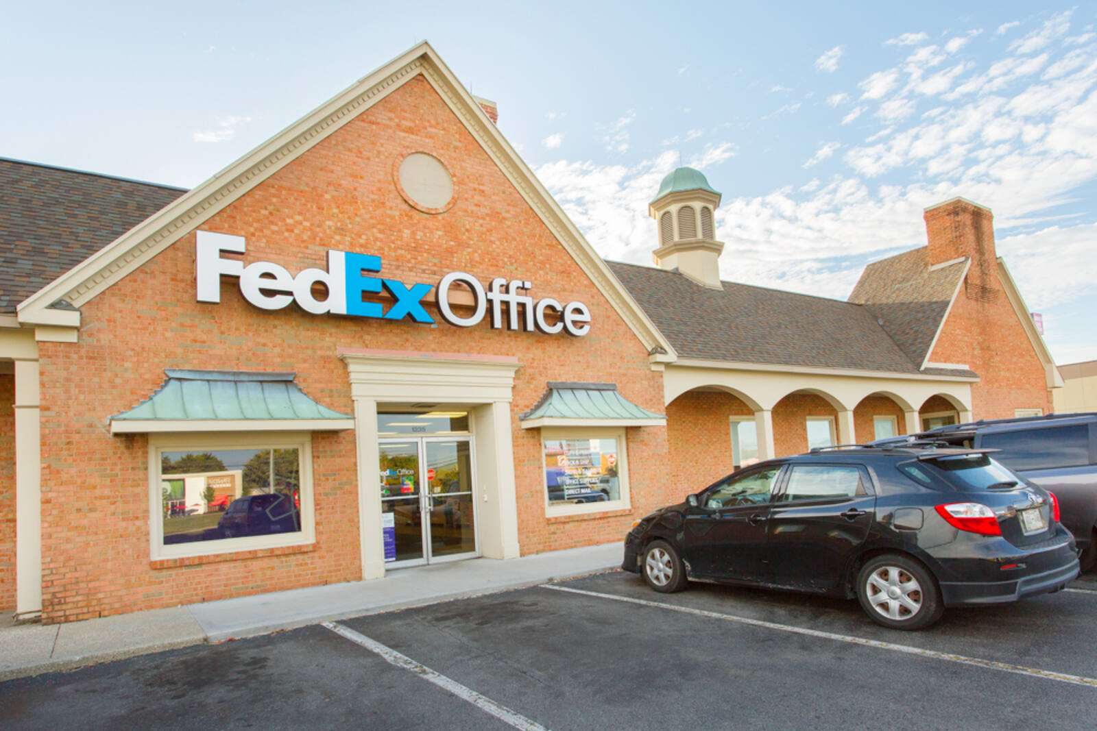 Dark grey hatchback parked in front of FedEx Office at Plainview Village shopping center 