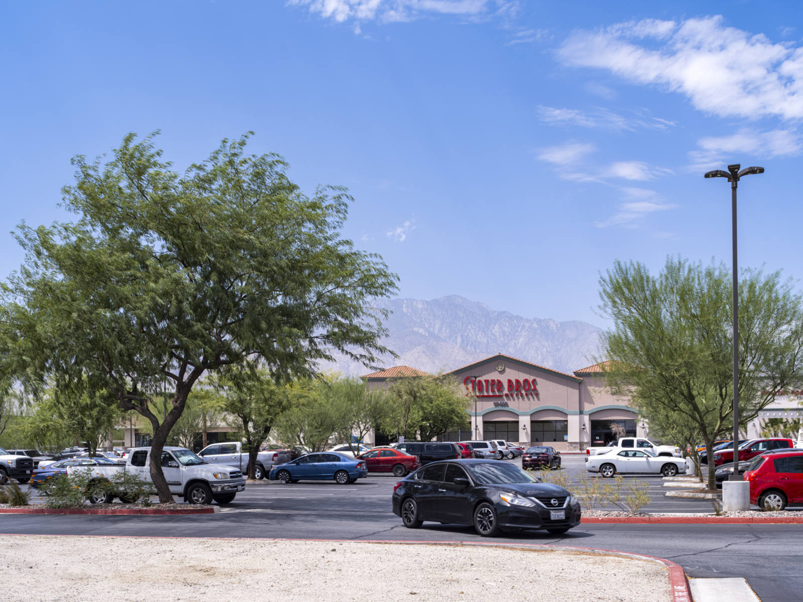 Black car driving through tree lined parking lot with Stater Bros. in the distance