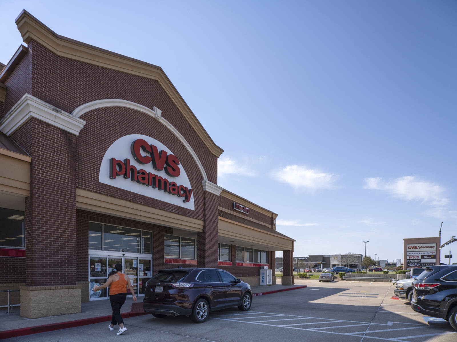 Woman enters CVS Pharmacy at front entrance with a car.