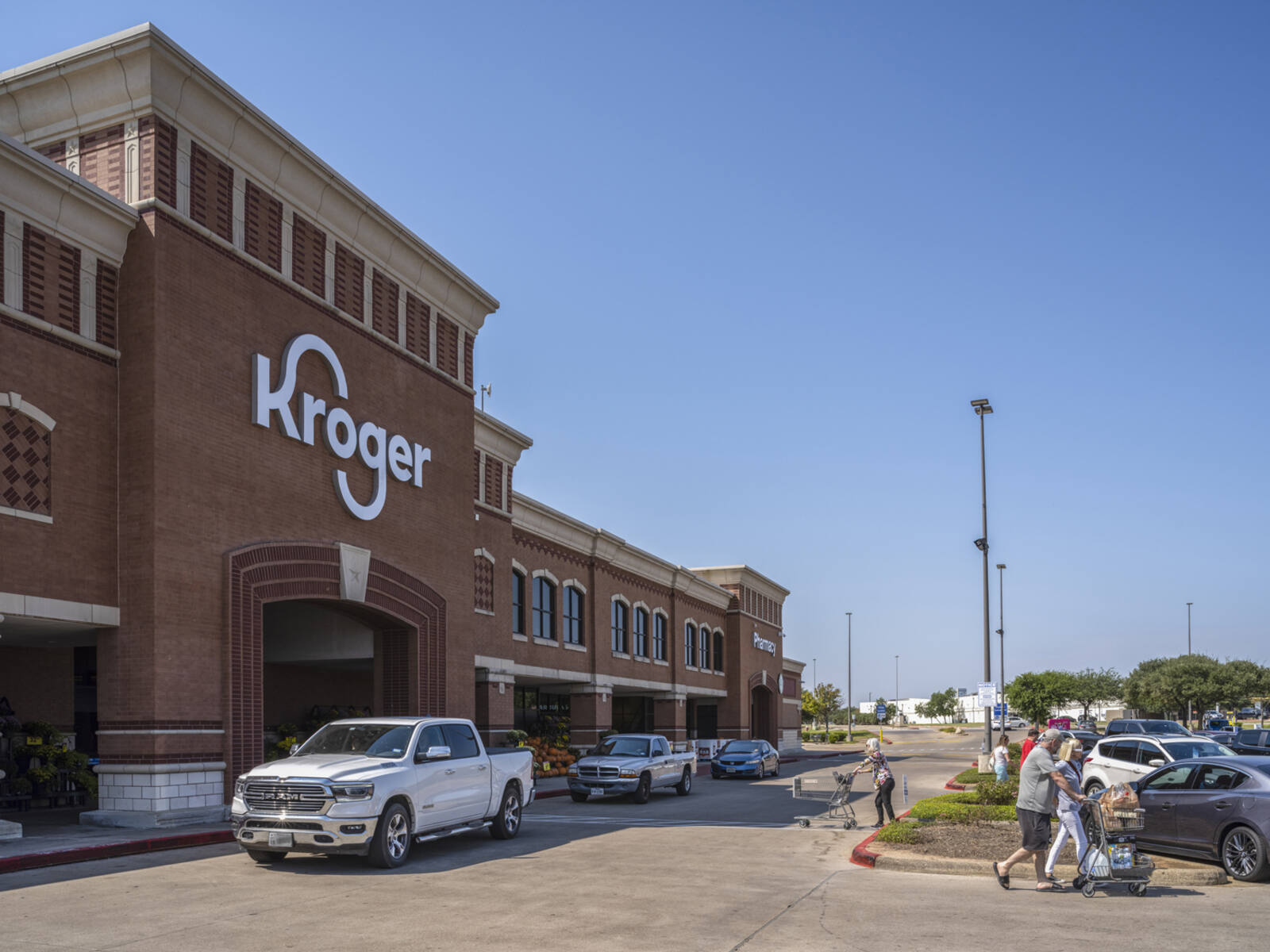 Customers with carts and a line of cars in front of Kroger Supermarket.