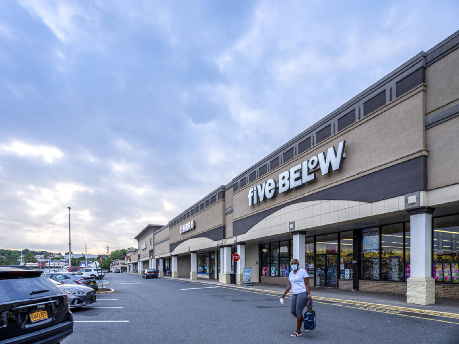 Person in white shirt and bag walking towards black SUV in front of Five Below