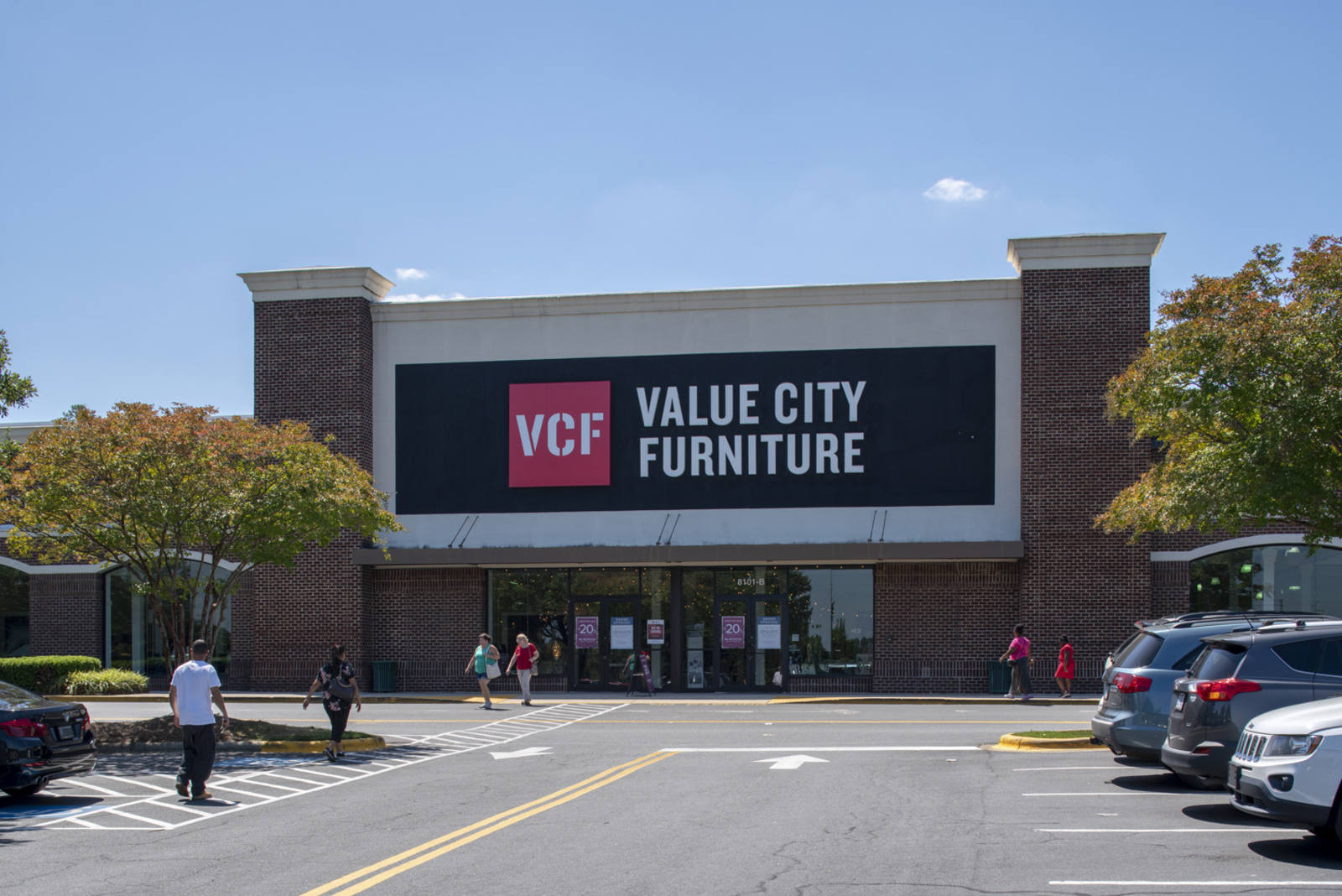 Trees on either side of Value City Furniture entrance with people walking in and out