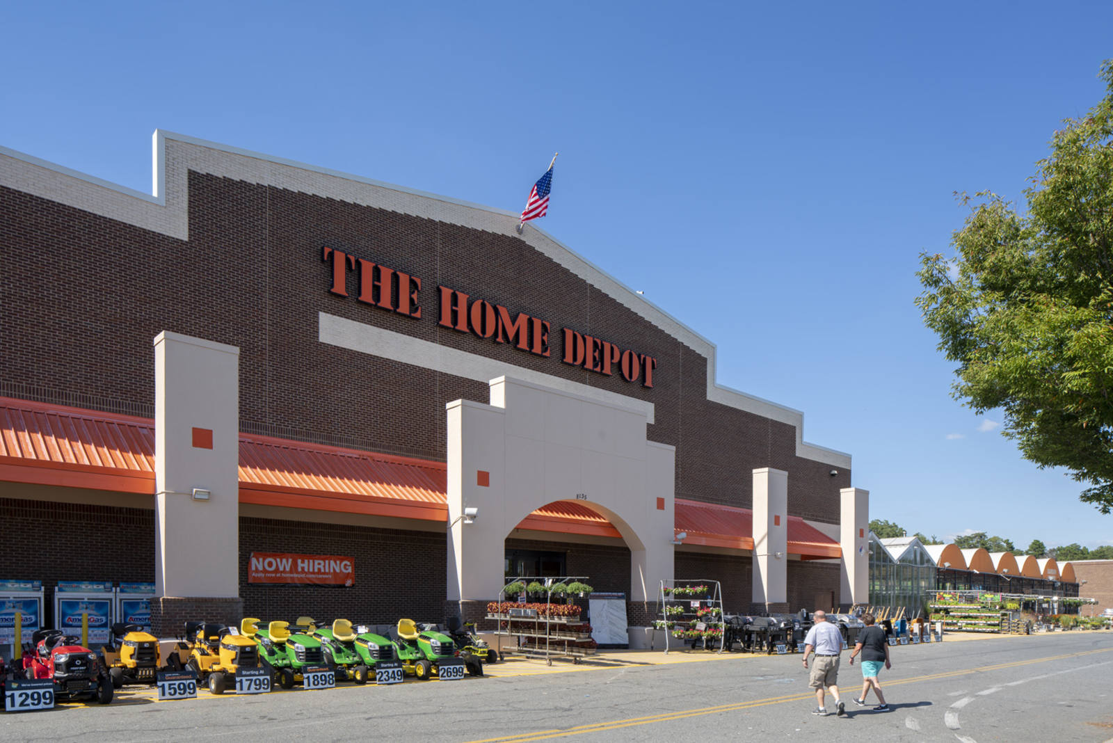Two people walking towards The Home Depot entrance with lawn mowers lining the front