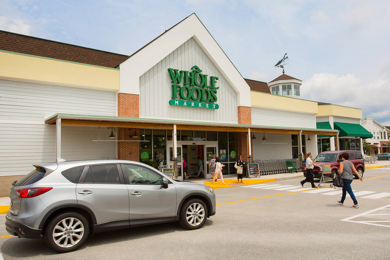 Silver SUV waiting as people walk into entrance of Whole Foods