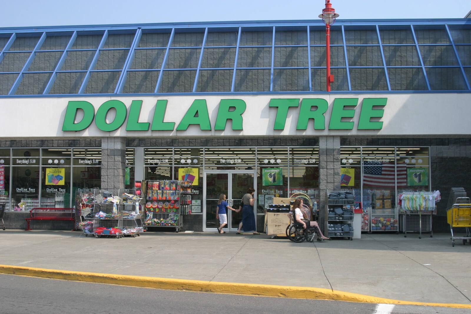 Woman and child and woman in wheel chair in front of Dollar entrance with merchandise out front