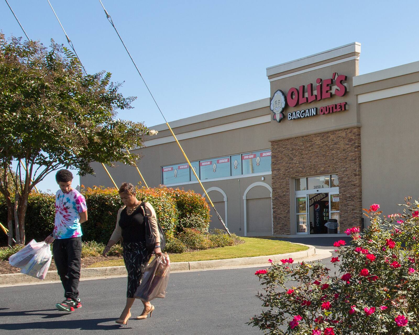 Two people walking on pavement away from Ollie's Bargain Outlet store