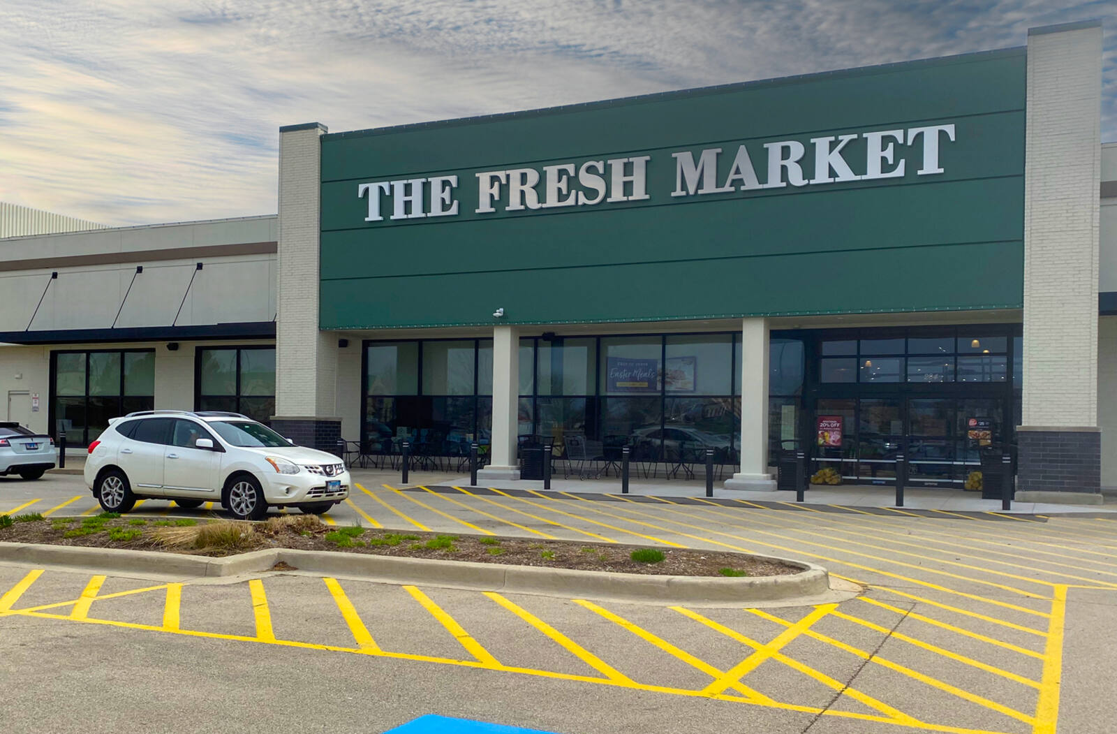 White SUV passing at entrance of The Fresh Market.